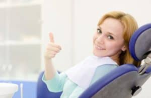 Woman sitting in a dental chair giving a thumbs up