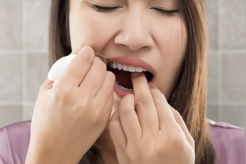 Woman flossing between teeth to remove any debris that may be causing sore gums