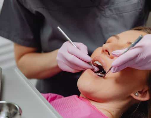 Headshot of a woman lying back with her mouth open will a hygienist examines her teeth